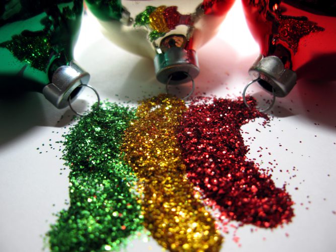 Three Christmas ornaments spilling glitter in green, gold, and red.