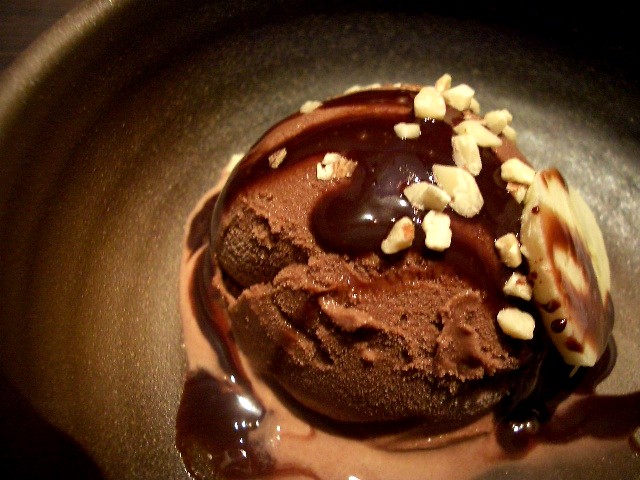 Image of scoop of chocolate ice cream, with fudge and chopped nuts in ceramic bowl
