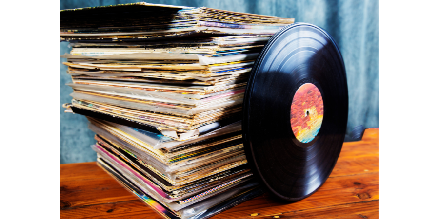 Image of a stack of beat up vinyl album covers, with a 78 rpm record leaning against it