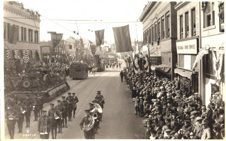 Image of Rose Parade Band marching in middle of street with crowds of spectators lining both sides of curbs/sidewalks (ca. 1925). Image source: http://pasadenadigitalhistory.com