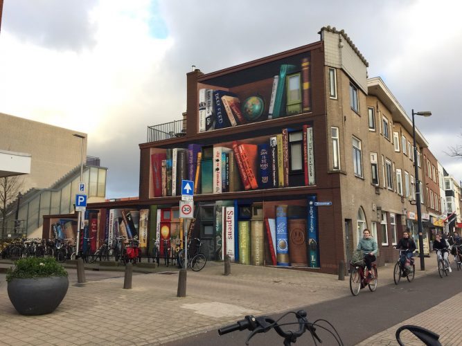 Image of Utrecht, Netherlands apartment building with one side painted to resemble a bookshelf stocked with local residents' recommended titles (street artist Jan Is De Man and tattoo artist Deef Feed)
