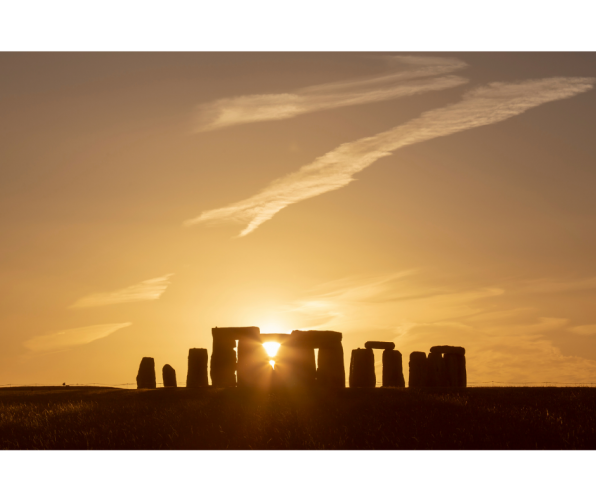 Photo of Stonehenge in silhouette, at sunset or sunrise, with sun shining through stones of the monument